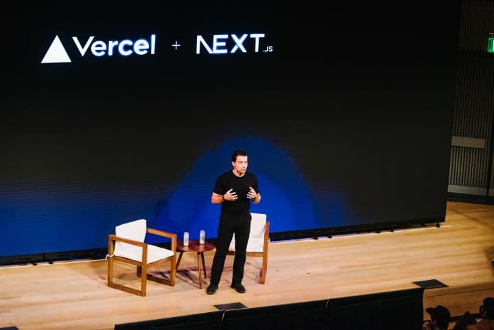 a man standing on a stage in front of a large screen