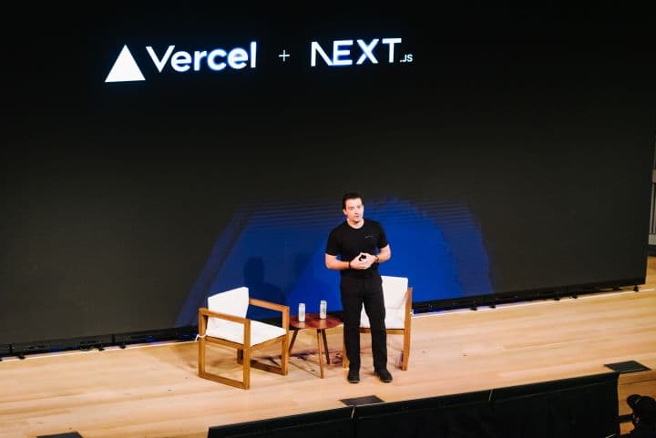 a man standing on a stage in front of a large screen