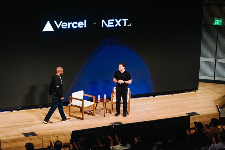 two men standing on a stage in front of a large screen