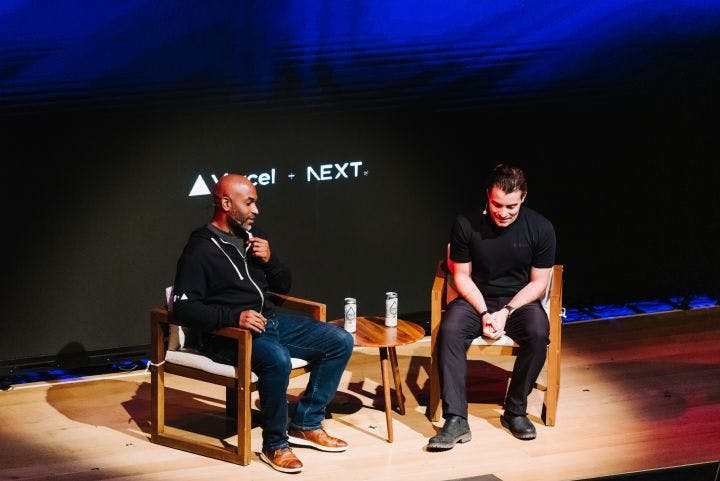 two men sitting in chairs talking on stage