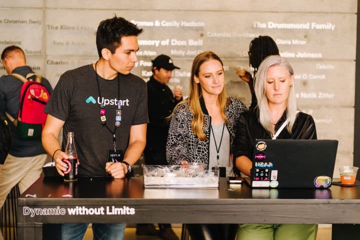 a group of people standing around a table with a laptop